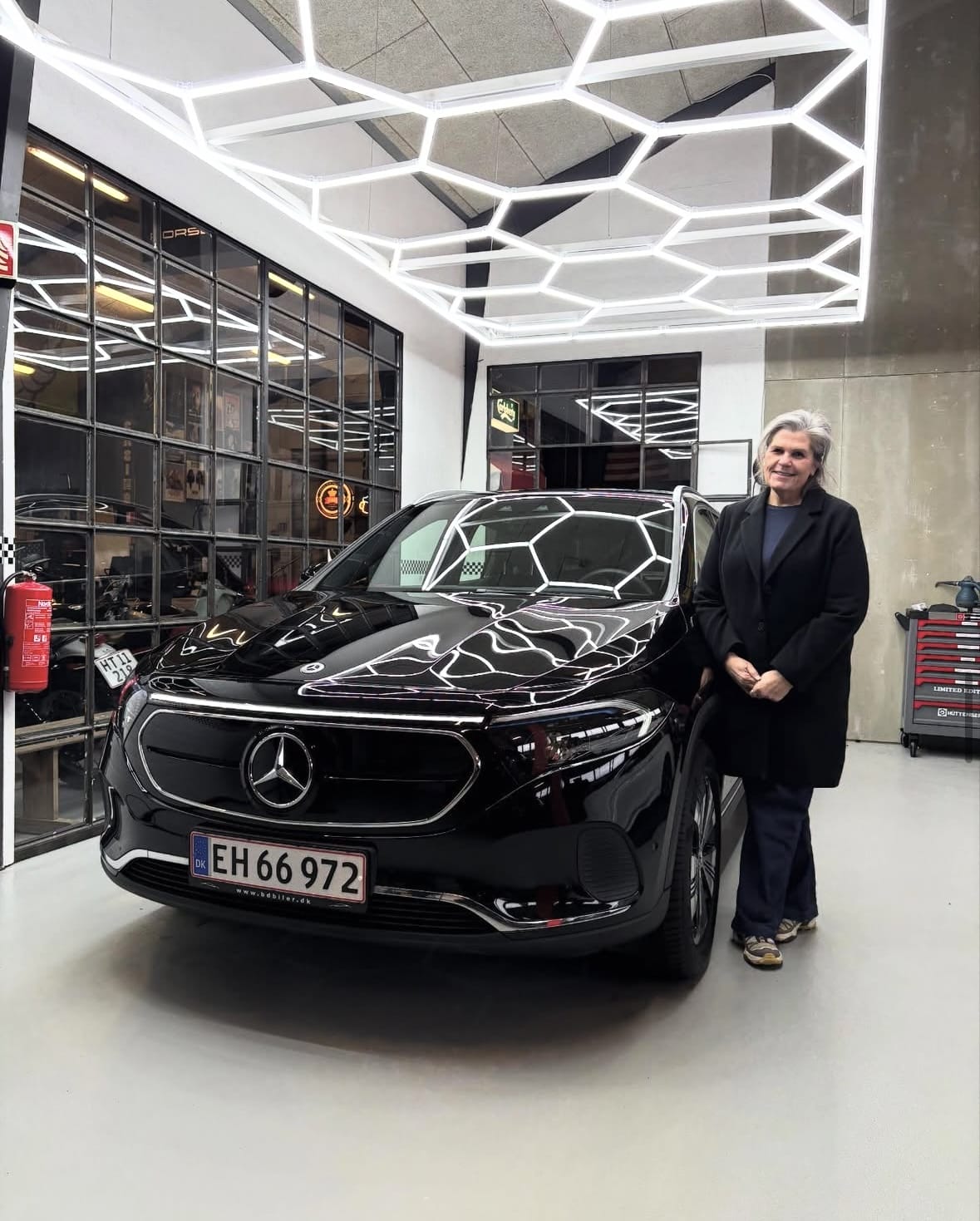 Kvinde står ved sort Mercedes i bilværksted