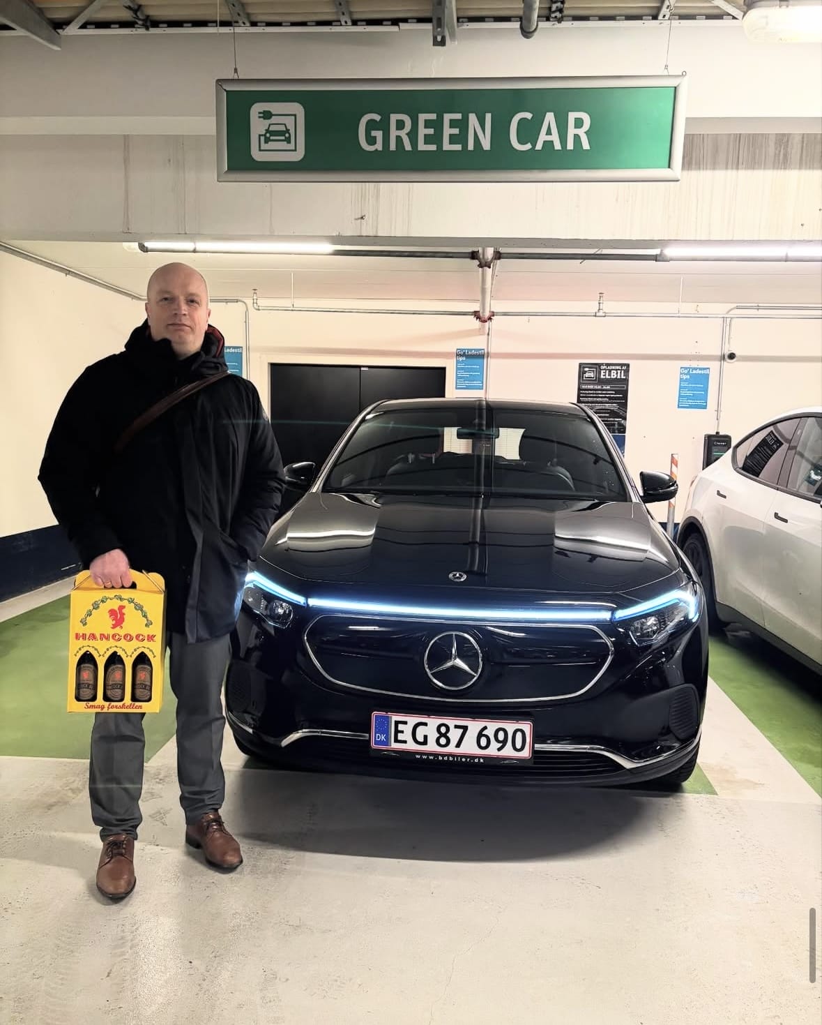 Mand ved sort elbil i grøn bil parkering