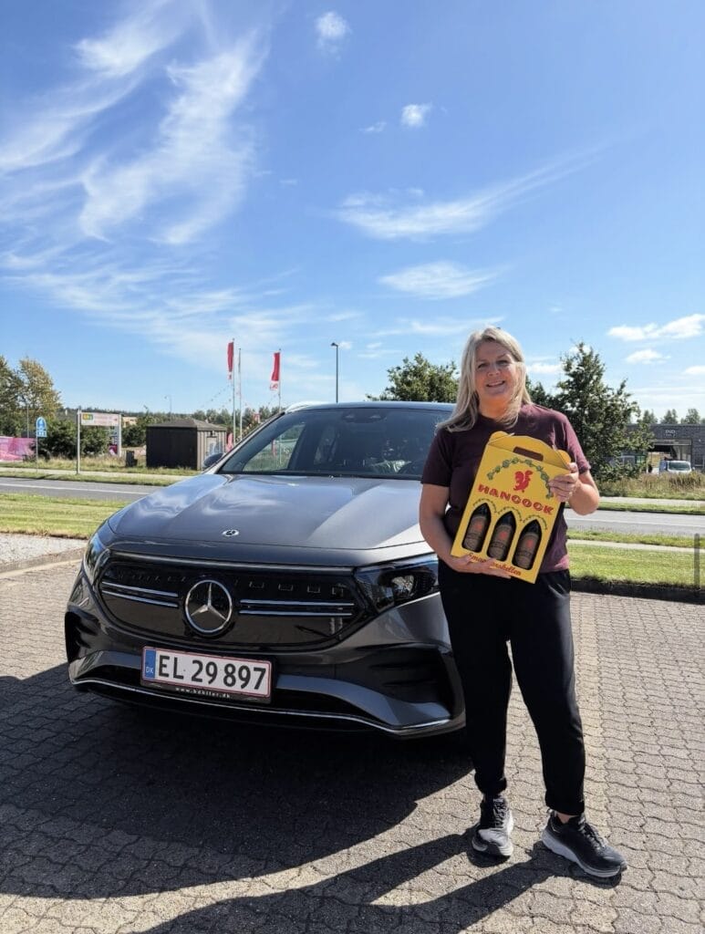 Kvinde foran sort Mercedes med gaveæske øl