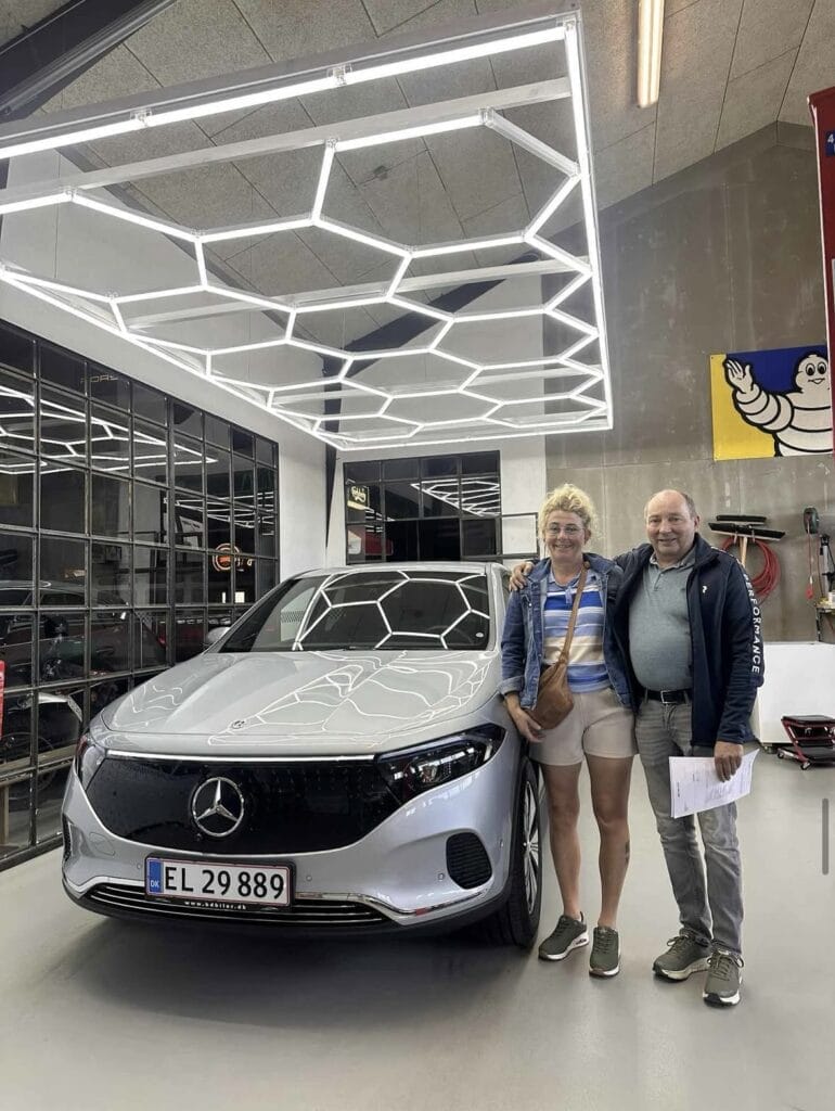 Par poserer med ny sølv Mercedes i garage